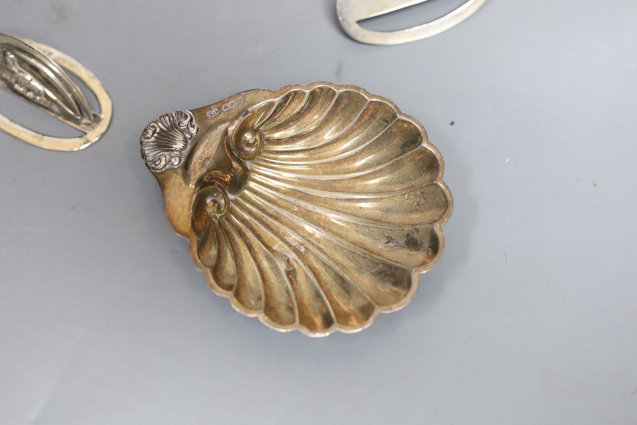 A pair of silver menu card holders, each decorated with a pheasant, Sampson Mordan & Co, Chester, 1907, width 59mm and a silver butter shell.